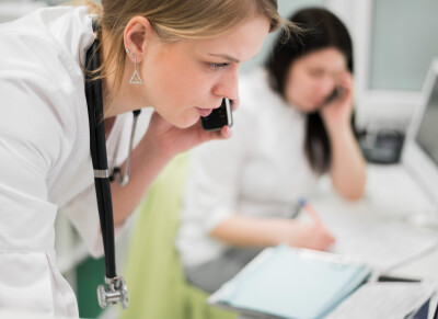 gros plan sur femme médecin répondant à un appel téléphonique, une autre personne féminine au téléphone est visible en arrière plan 