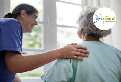 Infirmière riant avec une patiente âgée, de dos, et posant sa main sur son épaule