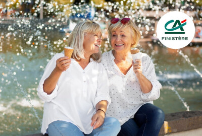 deux femmes seniors souriantes mangeant une glace en riant près d'une fontaine