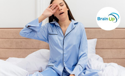jeune femme en pyjama bleu assisse dans son lit se réveillant en baillant