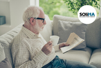 senior lisant son journal chez lui dans son canapé avec une tasse de boisson chaude à la main