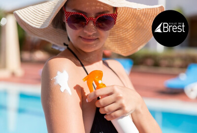 jeune femme avec lunettes de soleil et chapeau de paille se mettant de la crème solaire