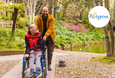 hommes se promenant dans un parc, l'un poussant le fauteuil de l'autre, en situation de handicap