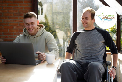 deux jeunes hommes dont un situation de handicap consultant un ordinateur portable en souriant