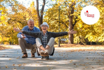 femme senior roulant assise sur un skate tandis que son conjoint la pousse