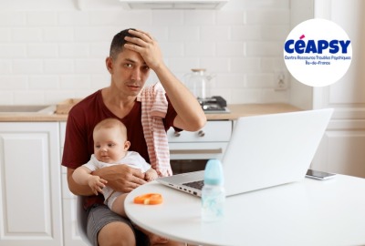 jeune père l'air épuisé se tenant le front, bébé sur ses genoux  et ordinateur portable sur la table devant lui