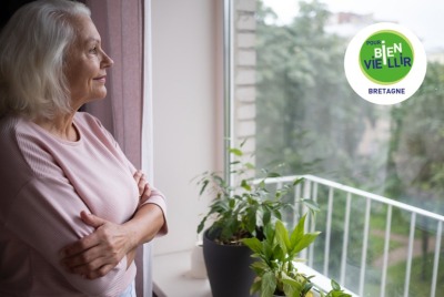 femme senior regardant par la fenêtre de sa maison avec un léger sourire