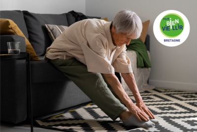 femme senior sur son canapé faisant des exercices d'étirements en essayant de se toucher le bout des pieds