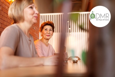 deux femmes assises à une table dont l'une regardant l'objectif avec le sourire