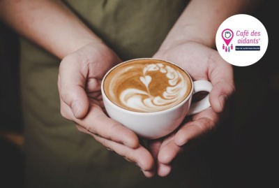 mains tenant une tasse de café avec formes de coeur dans la mousse