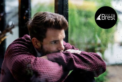 gros plan homme air soucieux tête posée sur ses bras croisé devant une fenêtre couverte de pluie