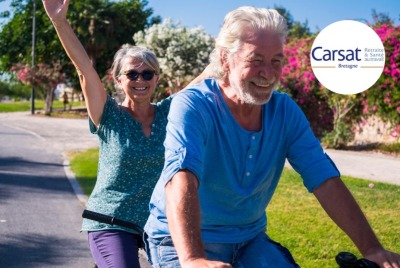 couple de seniors faisant du vélo, femme à l'arrière et levant les bras en l'air en souriant