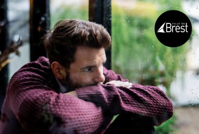 jeune homme tête enfouie dans ses bras regardant la pluie qui tombe par la fenêtre