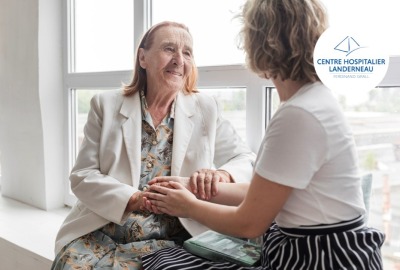 femme senior souriante tenant les mains d'une jeune femme de dos, devant une grande fenêtre