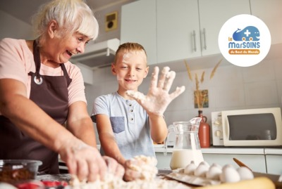 grand-mère préparant une recette avec son petit-fils et riant parce qu'il a de la pâte plein les doigts