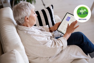 femme senior lisant sur une tablette, assise dans son canapé