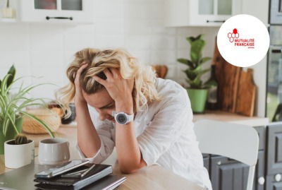 jeune femme épuisée se tenant la tête dans les mains assise à une table, avec ses agendas et son téléphone devant elle