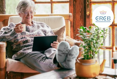 femme senior chez elle en hiver, une tasse à la main, assise dans un fauteuil et regardant une tablette