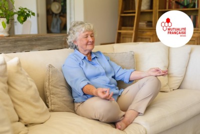 femme senior méditant, les yeux fermés sur son canapé