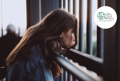 jeune femme l'air triste tête posée sur une barrière métallique et regardant au loin