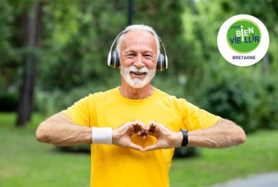 homme senior à l'extérieur en tenue de sport avec casque de musique sur les oreilles, formant le symbole d'un coeur sur son torse avec ses mains