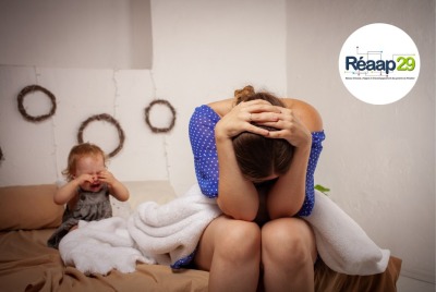 mère épuisée se tenant la tête entre les mains pendant que son enfant pleure sur le lit derrière elle