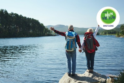 couple de seniors, de dos, devant un lac, en tenue de randonnée