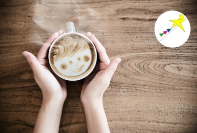 gros plan mains tenant une tasse de boisson chaude dont la mousse forme un visage souriant
