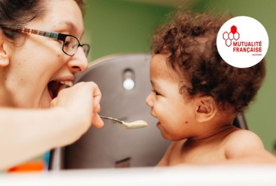 maman faisant des grimaces à son enfant pendant qu'elle le nourrit avec une petite cuillère