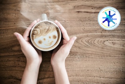 gros plan mains tenant une tasse de boisson chaude dont la mousse forme un visage souriant